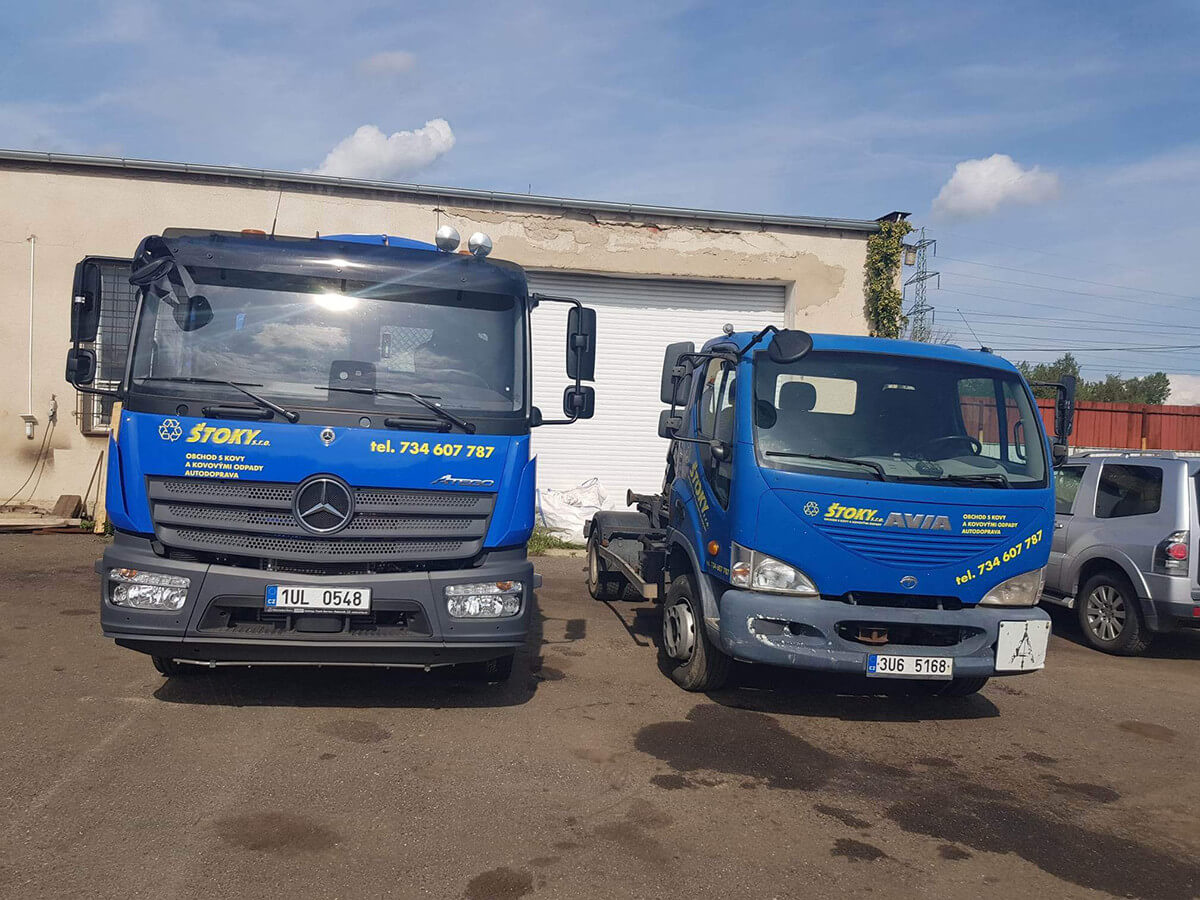 dvě modrá nákladní auta s logem ŠTOKY stojící vedle sebe